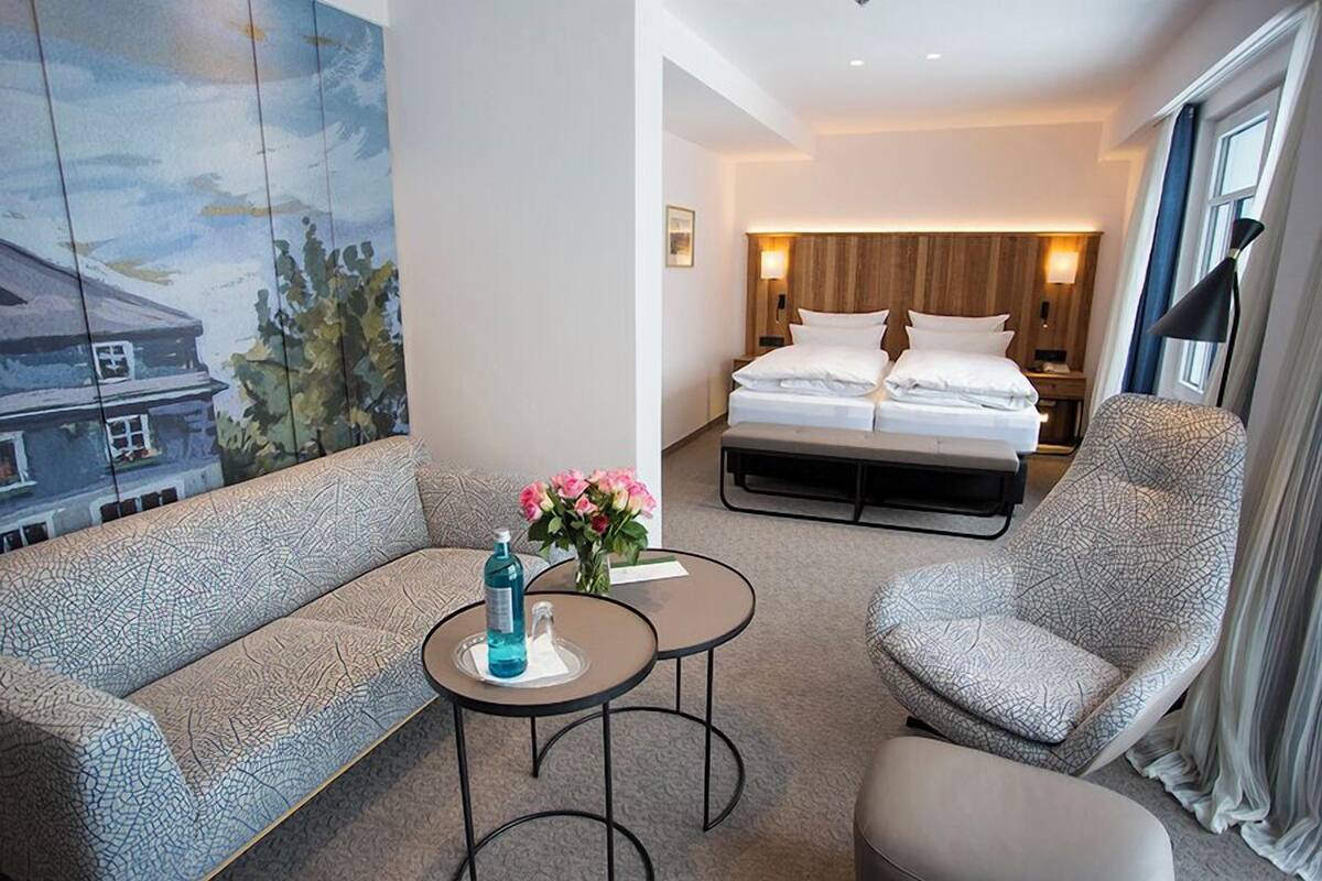 A hotel room with a bed, a sofa, a chair, and a small table with a vase of flowers.