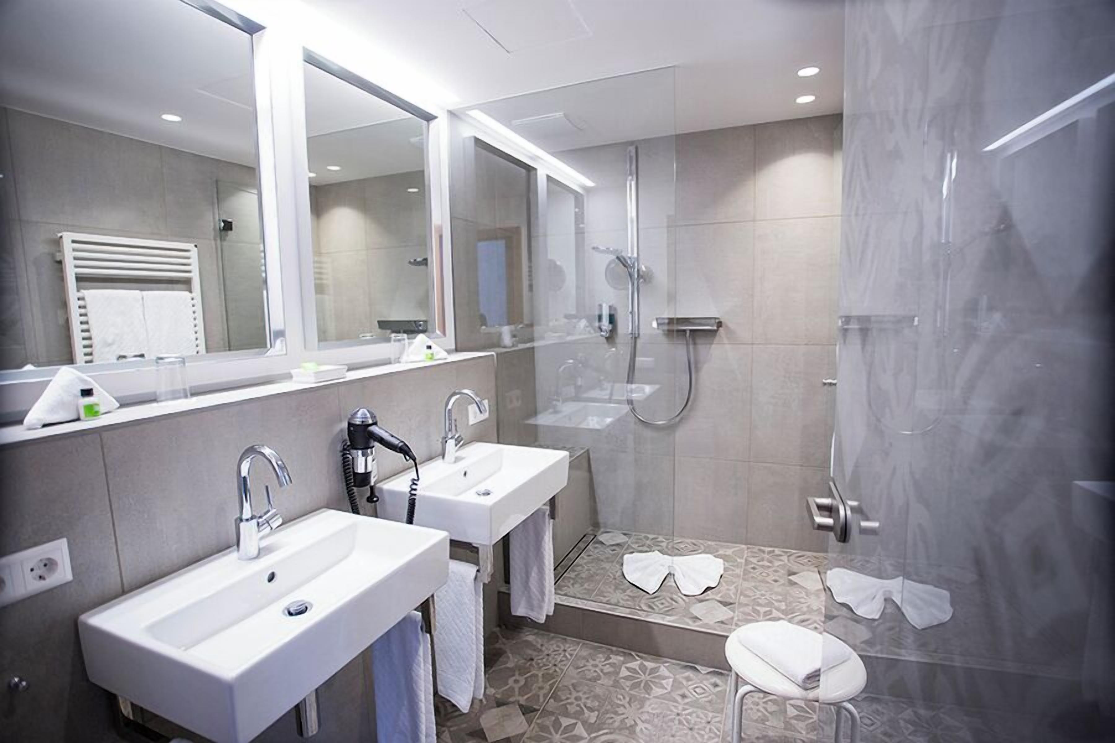 A modern bathroom with two sinks, a large mirror, and a walk-in shower.