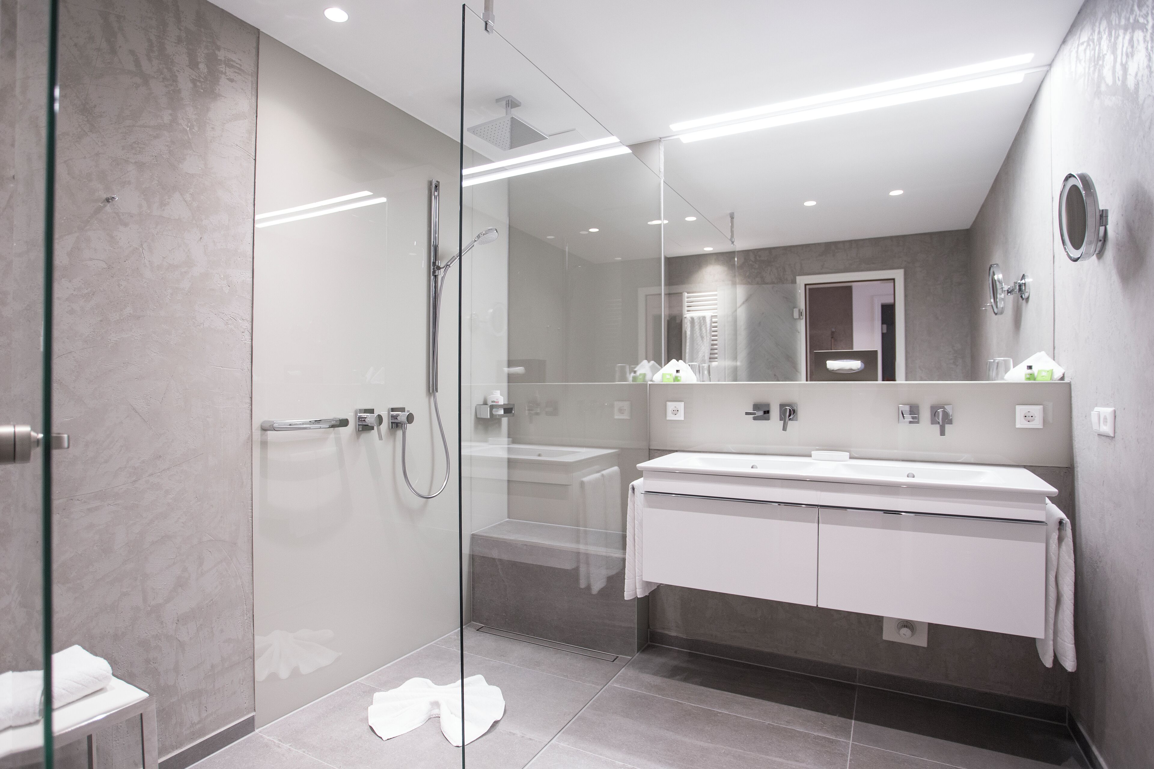 A modern bathroom with a glass-enclosed shower, a white vanity with a large mirror, and a tiled floor.