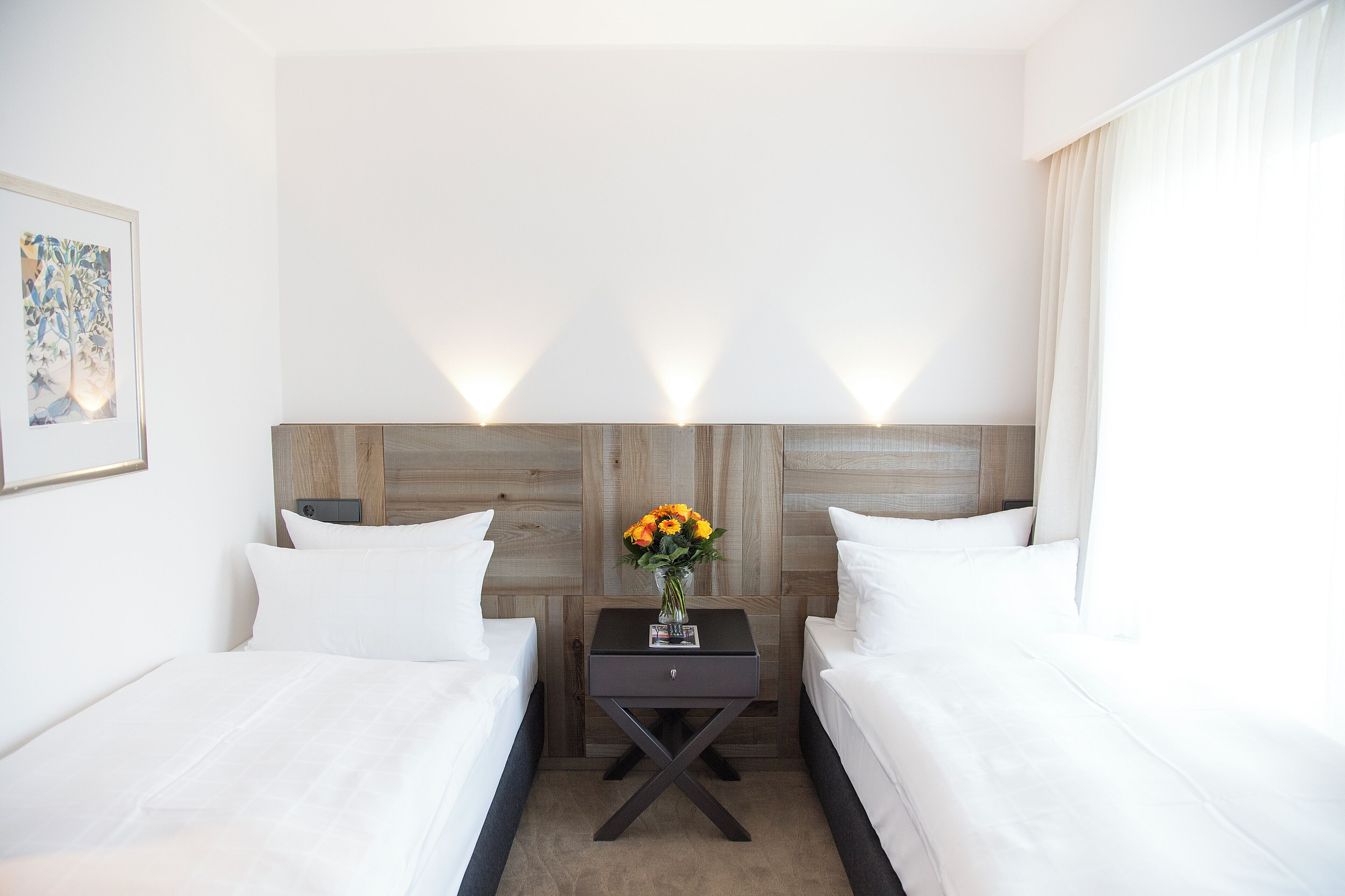 A hotel room with two beds, a nightstand with a vase of flowers, and a framed picture on the wall.