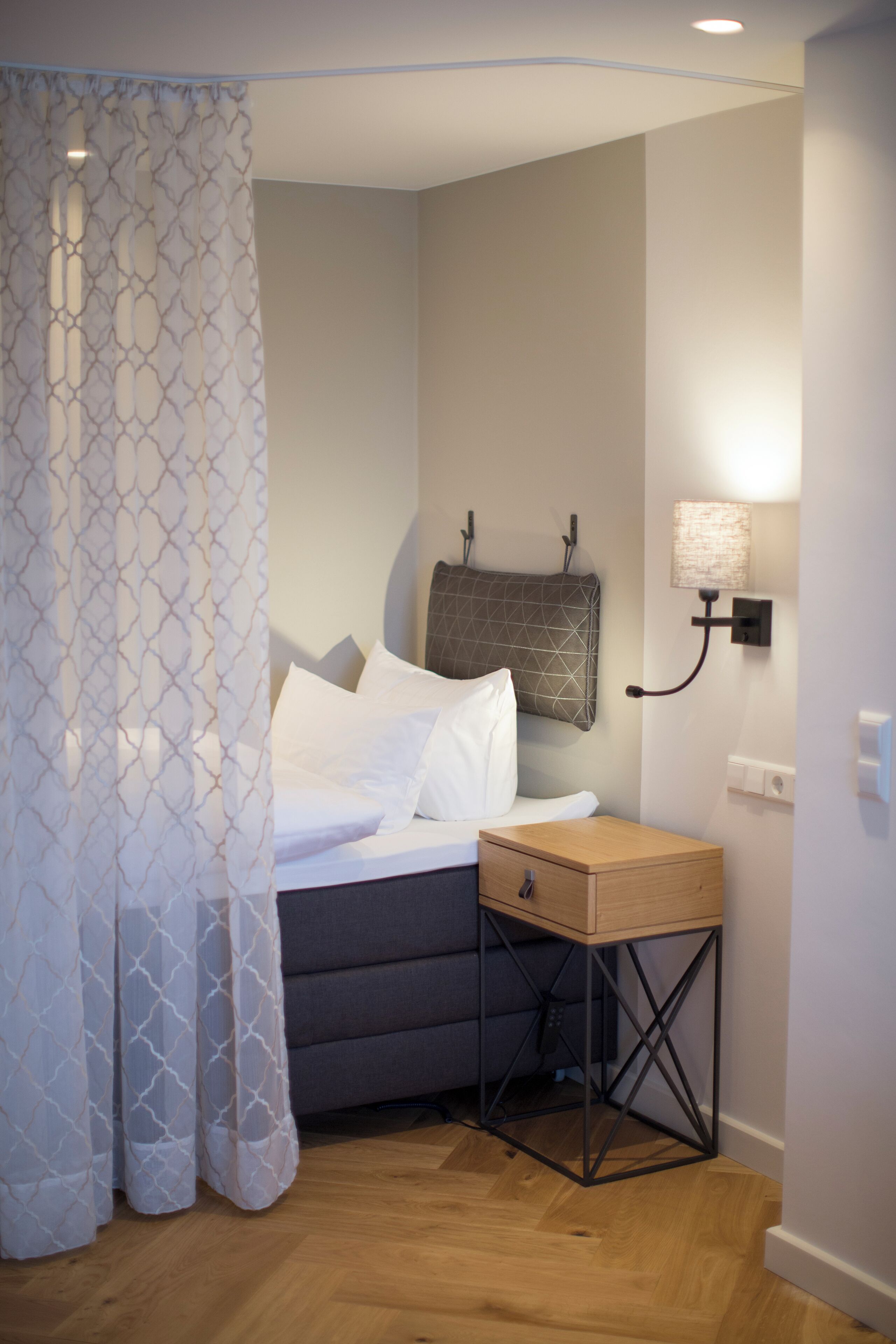 A bedroom with a bed, a bedside table, a lamp, and a curtain.