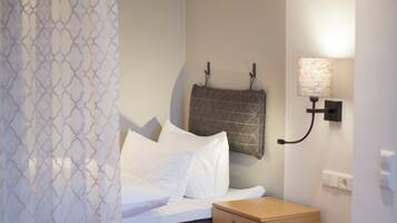 A bedroom with a bed, a bedside table, a lamp, and a curtain.