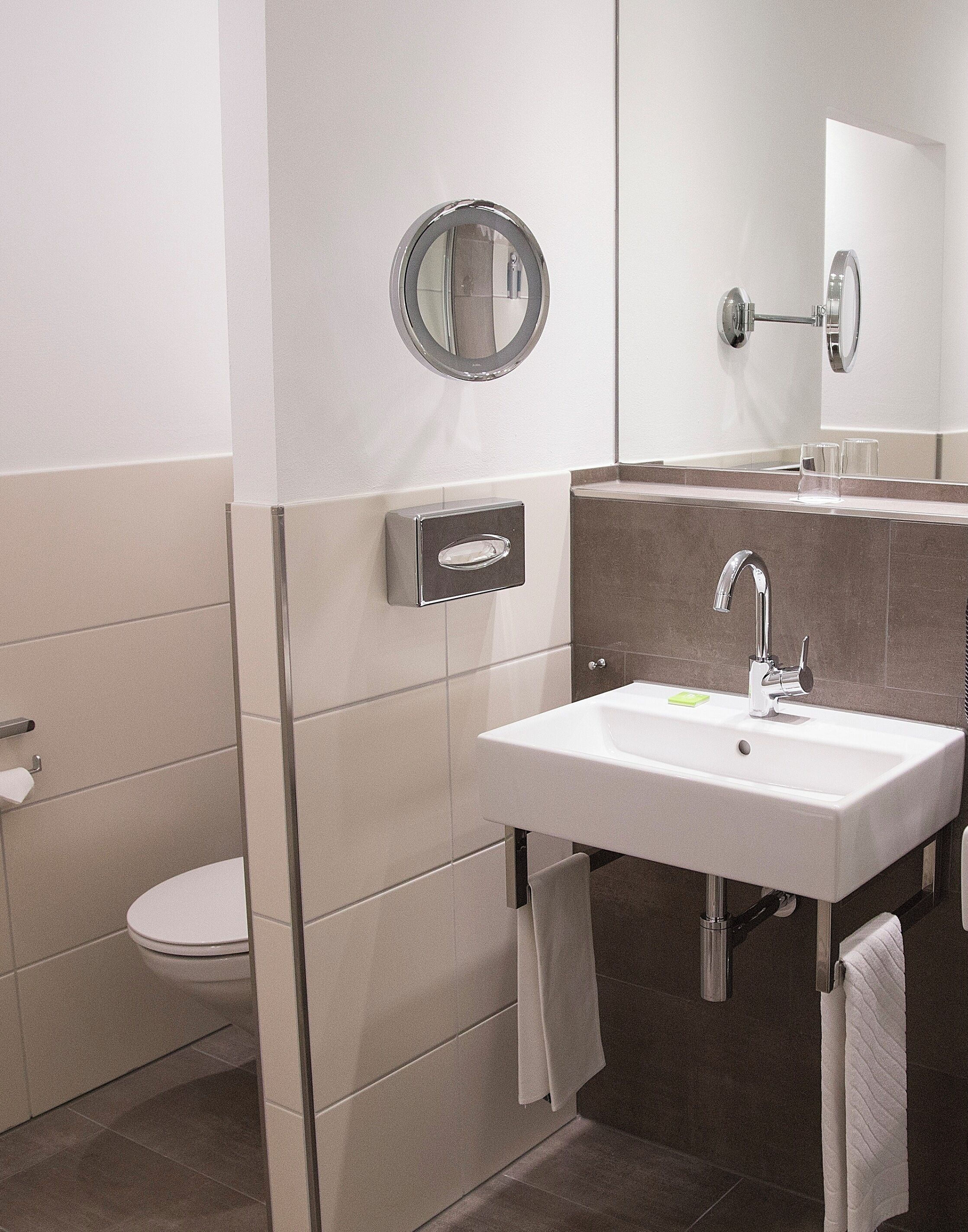 A modern bathroom with a white sink, a mirror, and a toilet.