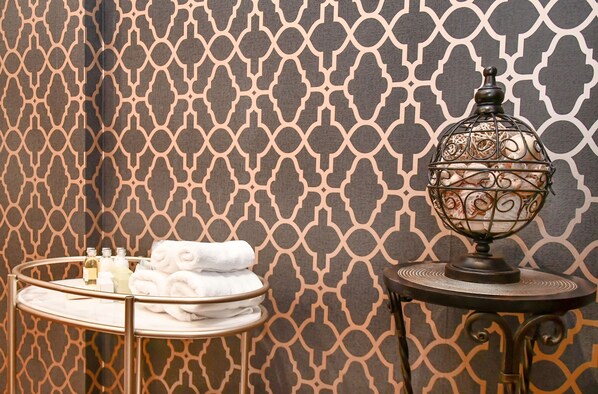 Une salle de bain avec un mur orné d’un motif, un plateau contenant des serviettes et des articles de toilette, et une lampe décorative.