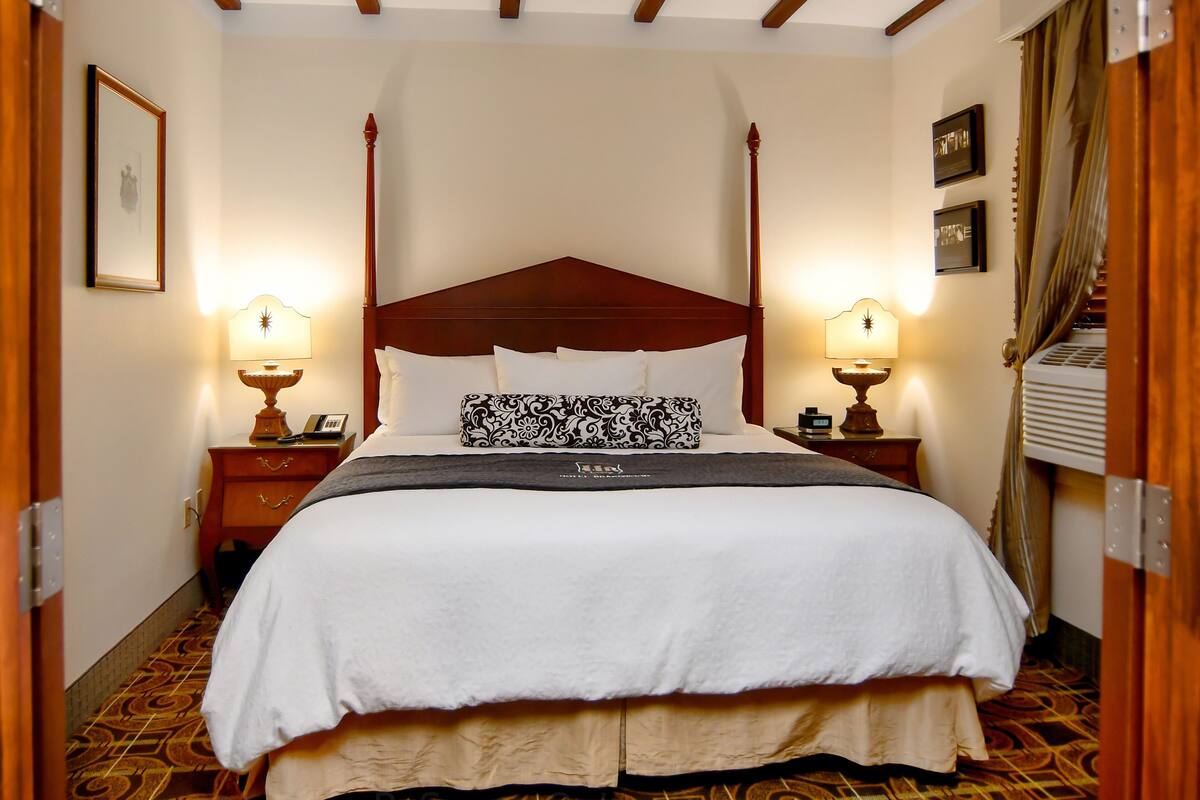 Un dormitorio con una cama grande, cabecera de madera, dos mesitas de noche con lámparas, almohadas estampadas y una alfombra con diseño.
