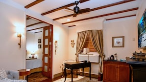 A hotel room with a bed, a desk, a chair, a sofa, a ceiling fan, and a window with curtains. - Brand Plaza Hotel (Glendale)