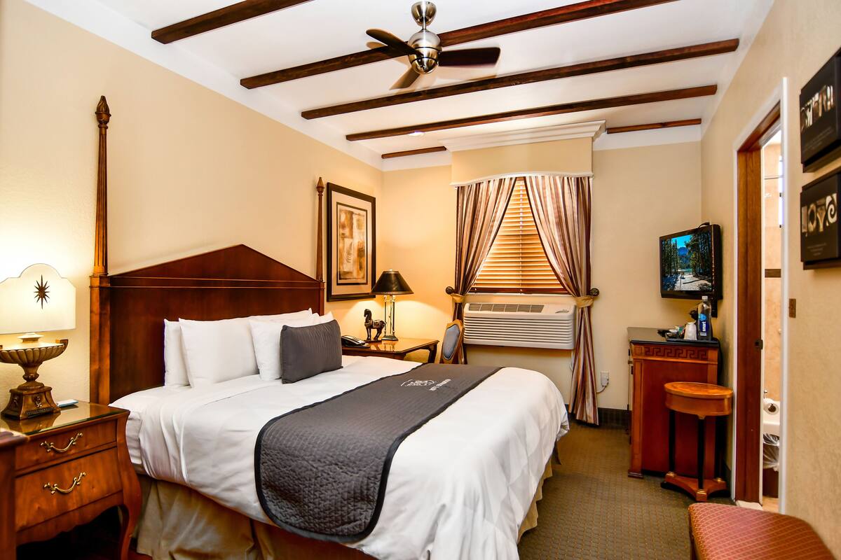 Una habitación de hotel con cama, mesita de noche, lámpara, aire acondicionado y televisor.