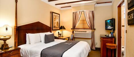 A hotel room with a bed, bedside table, lamp, air conditioning unit, and a television.