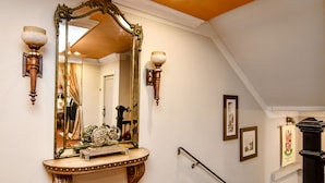 A staircase with ornate wall sconces, a large mirror, and a framed picture. - Brand Plaza Hotel (Glendale)