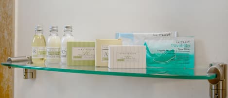 Estante de vidrio con diversos artículos de aseo personal, incluyendo botellas de champú, acondicionador y un kit de limpieza de zapatos de tamaño de viaje.