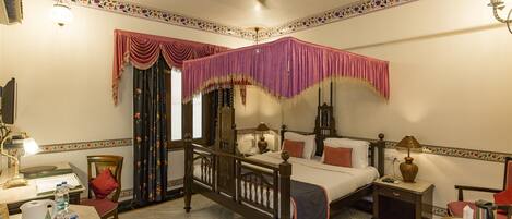 A four-poster bed with a canopy, a desk with a lamp, a chair, and a small table with a kettle.