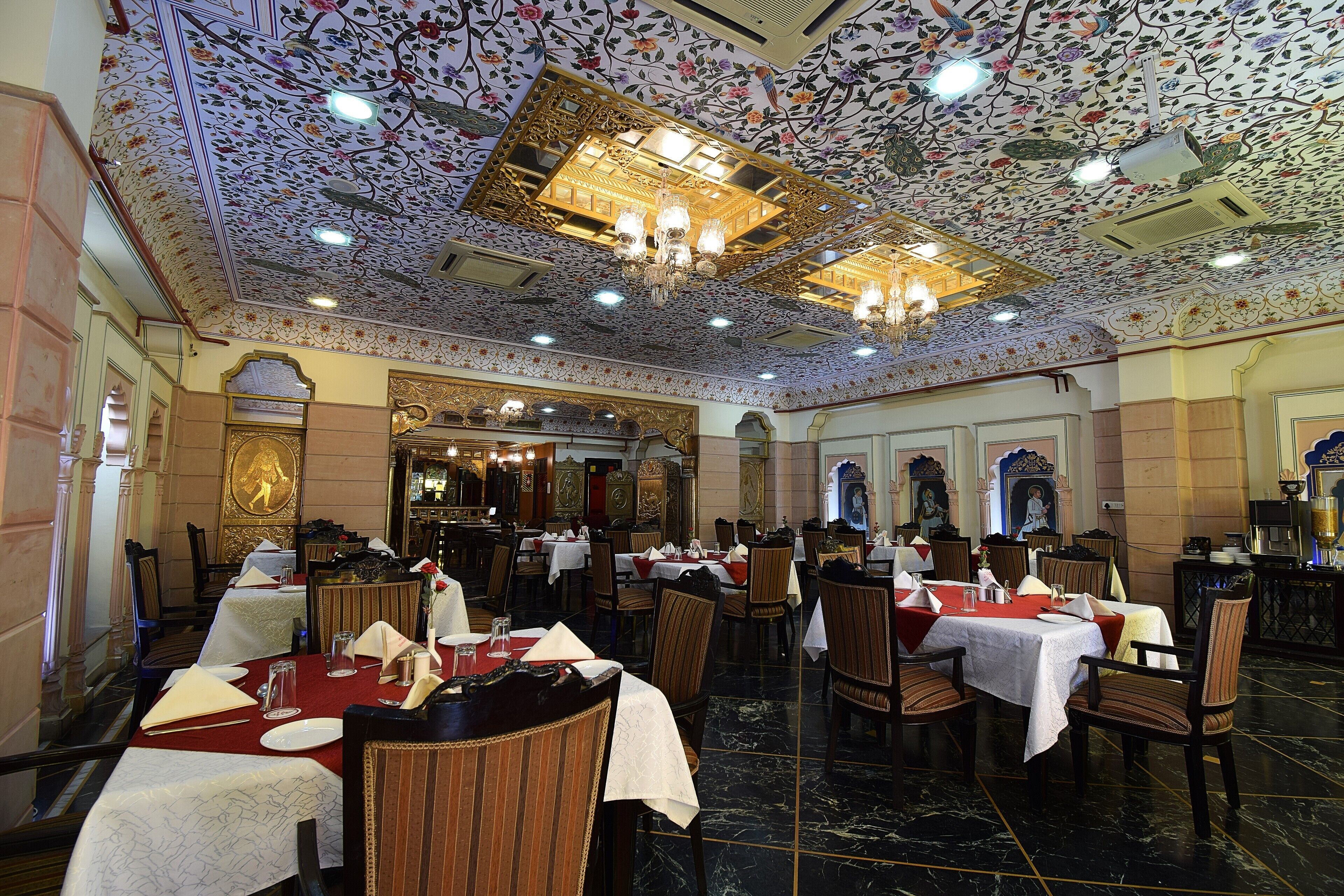 A restaurant with tables set for dining, chandeliers, and ornate ceiling decorations.