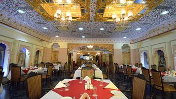 A dining area with tables set for four, ornate chandeliers, and a patterned ceiling.