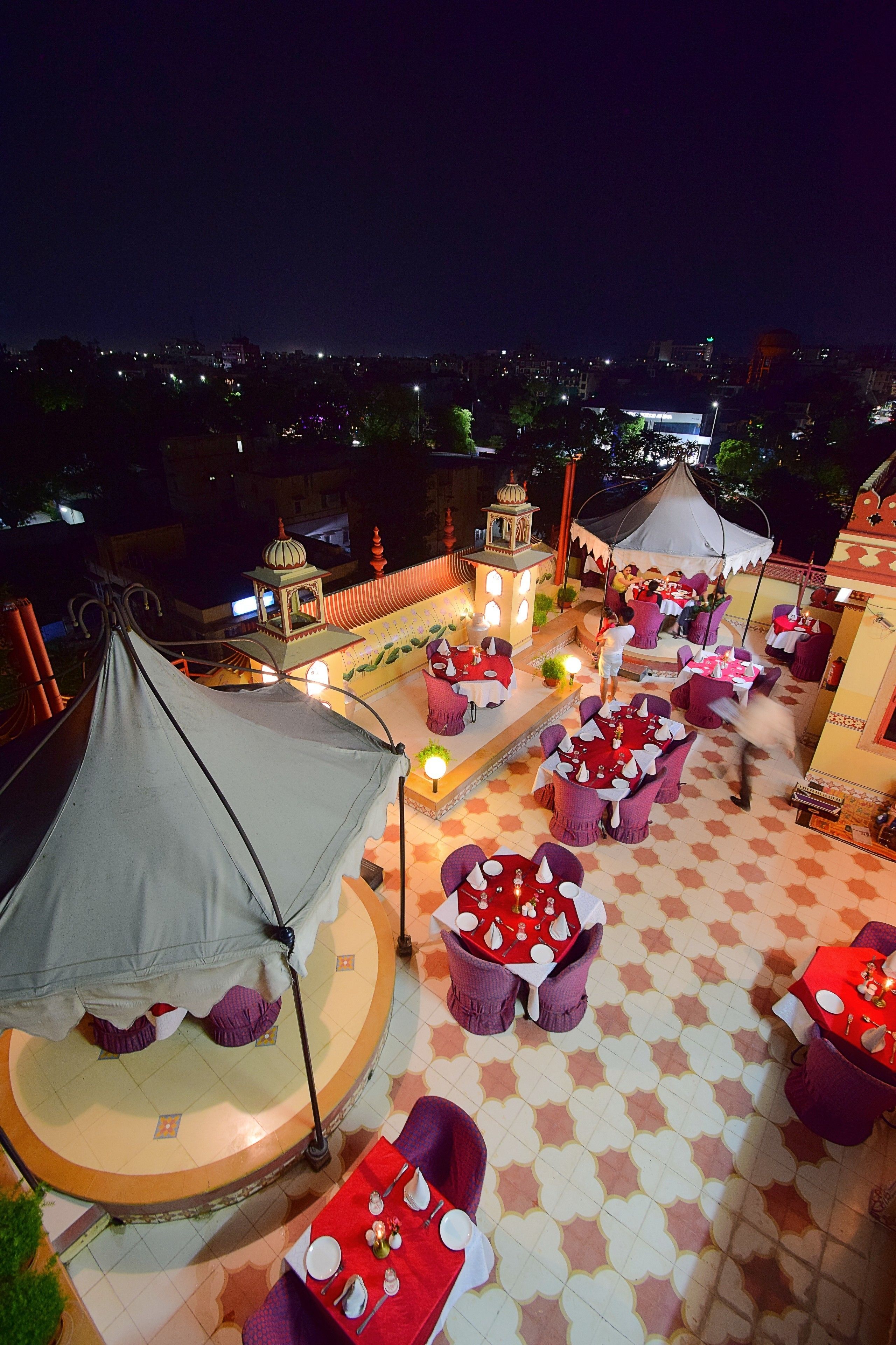 Una terraza en la azotea con mesas y sillas redondas, una carpa y un edificio decorativo al fondo.