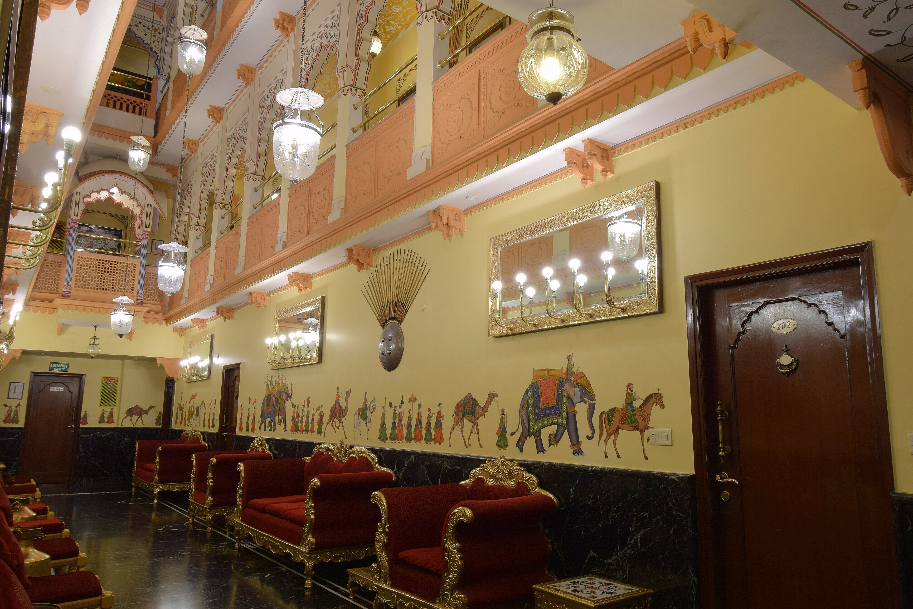 Un salón imponente con candelabros ornamentados, sillas de terciopelo rojo y un mural que representa una escena histórica.