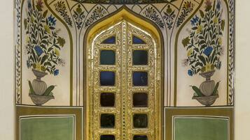 Um quarto com um arco decorativo, uma porta grande e elaborada, e dois painéis laterais com motivos florais.