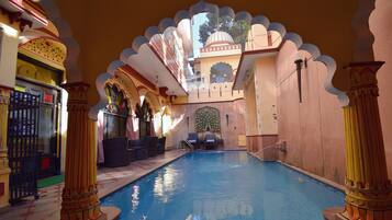 An indoor swimming pool with ornate arches and columns, a seating area, and a view of the sky.
