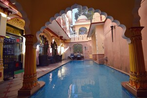 Piscina interior com arcos e colunas elaborados, área de estar e vista do céu.