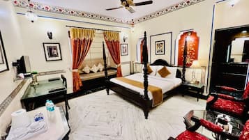 A hotel room with a four-poster bed, a sitting area with a red upholstered chair, a small table, and a ceiling fan.