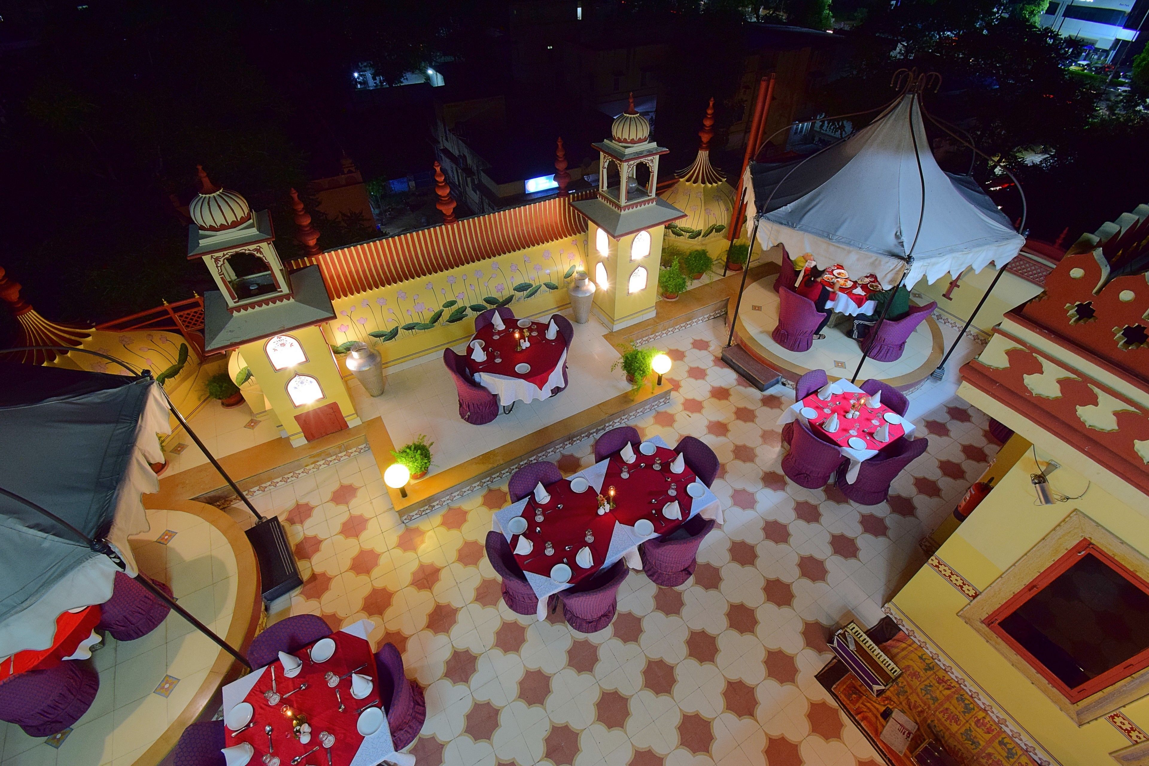 A rooftop terrace with multiple dining tables and chairs, surrounded by decorative elements and a small garden area.