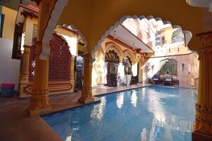 Ein Innenpool mit verzierten Bögen und Säulen, ein Sitzbereich mit Stühlen und einem Tisch sowie eine Zierfontäne.