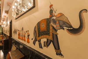Parede com um mural grande de um elefante e um homem montando nele, um espelho e uma moldura com uma foto de pessoas.