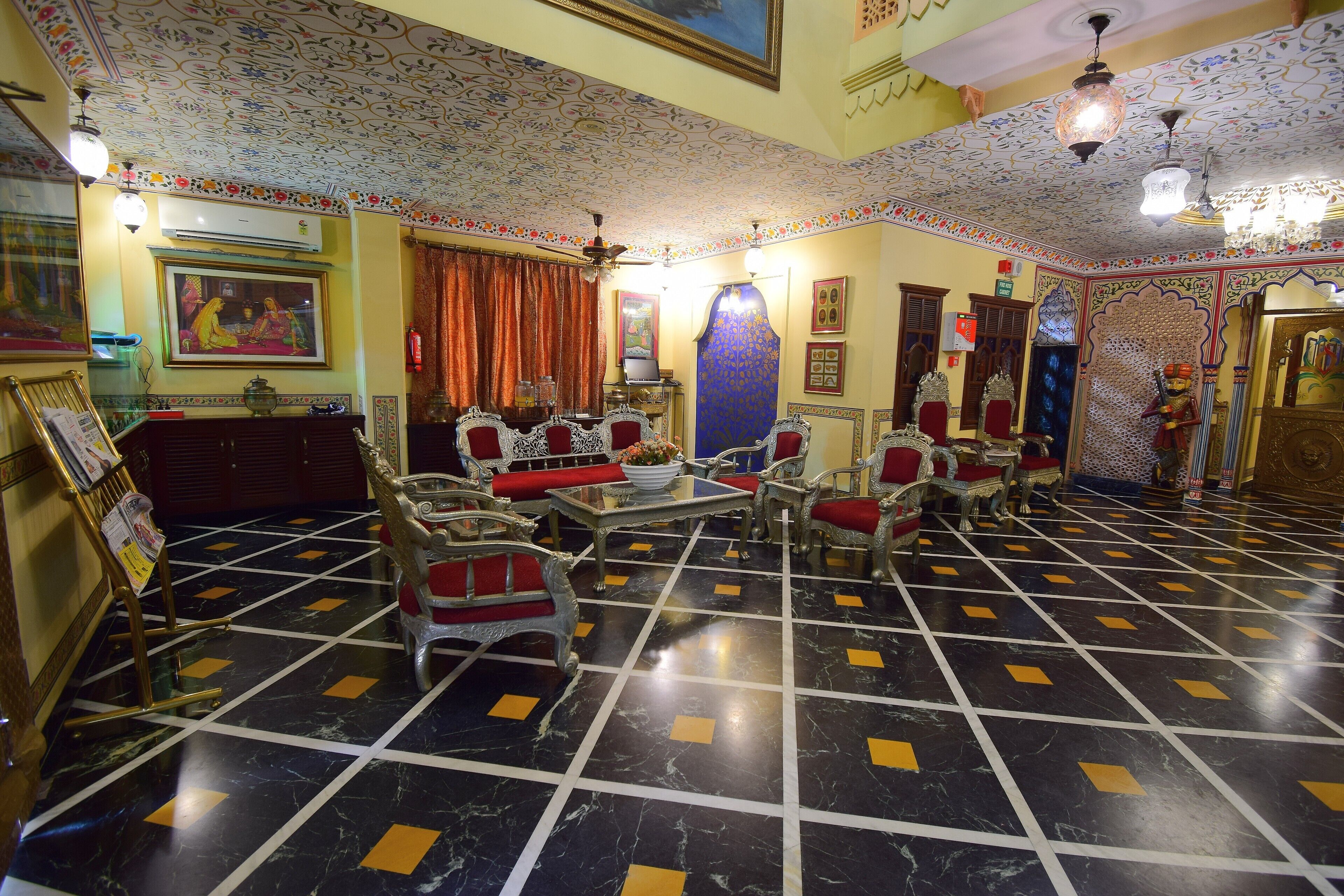 A traditional room with patterned ceiling, a chandelier, and a large blue vase.