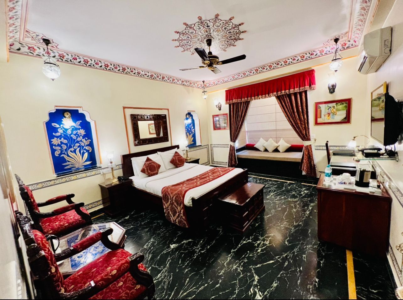 A hotel room with a bed, a desk, a chair, a ceiling fan, and a decorative wall piece.