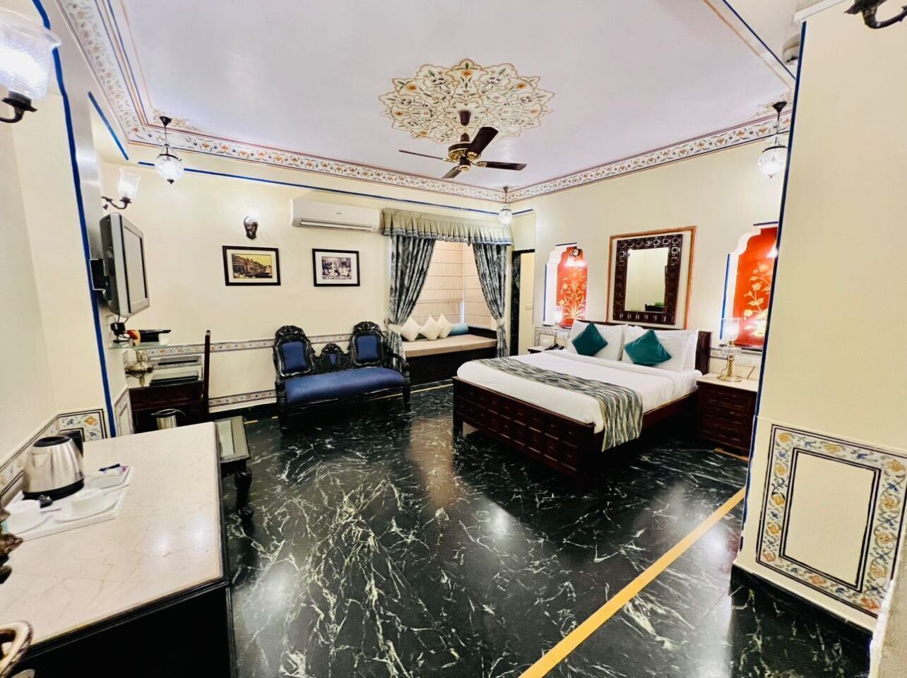 A hotel room with a bed, a desk, a chair, a ceiling fan, and a decorative ceiling.