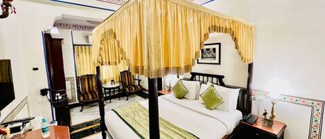 A four-poster canopy bed with a green throw, a nightstand with a lamp, and a chair in a hotel room.