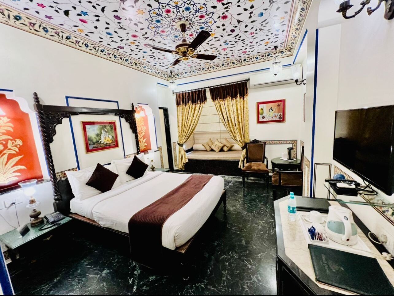 Una habitación de hotel con cama, escritorio, silla, televisor y ventilador de techo.