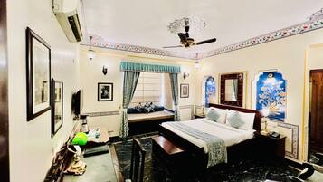 Quarto de hotel com cama, escrivaninha, cadeira, ventilador de teto e janela com cortinas.