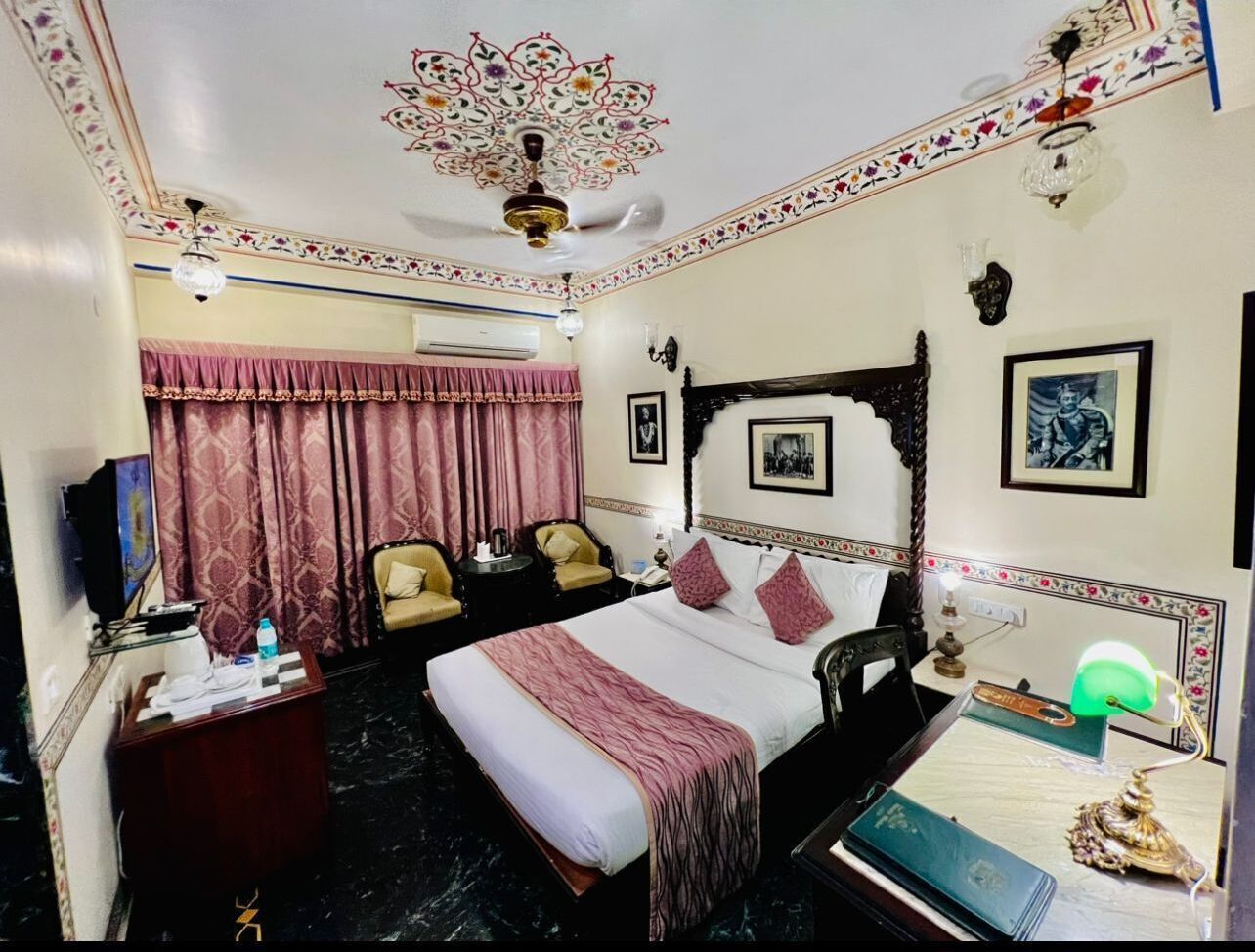 Una habitación de hotel con una cama grande, dos sillas, un escritorio, un televisor y un ventilador de techo.