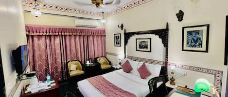 Una habitación de hotel con una cama grande, dos sillas, un escritorio, un televisor y un ventilador de techo.