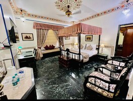 Quarto de hotel com uma cama, área de estar com cadeiras, escrivaninha e televisão.