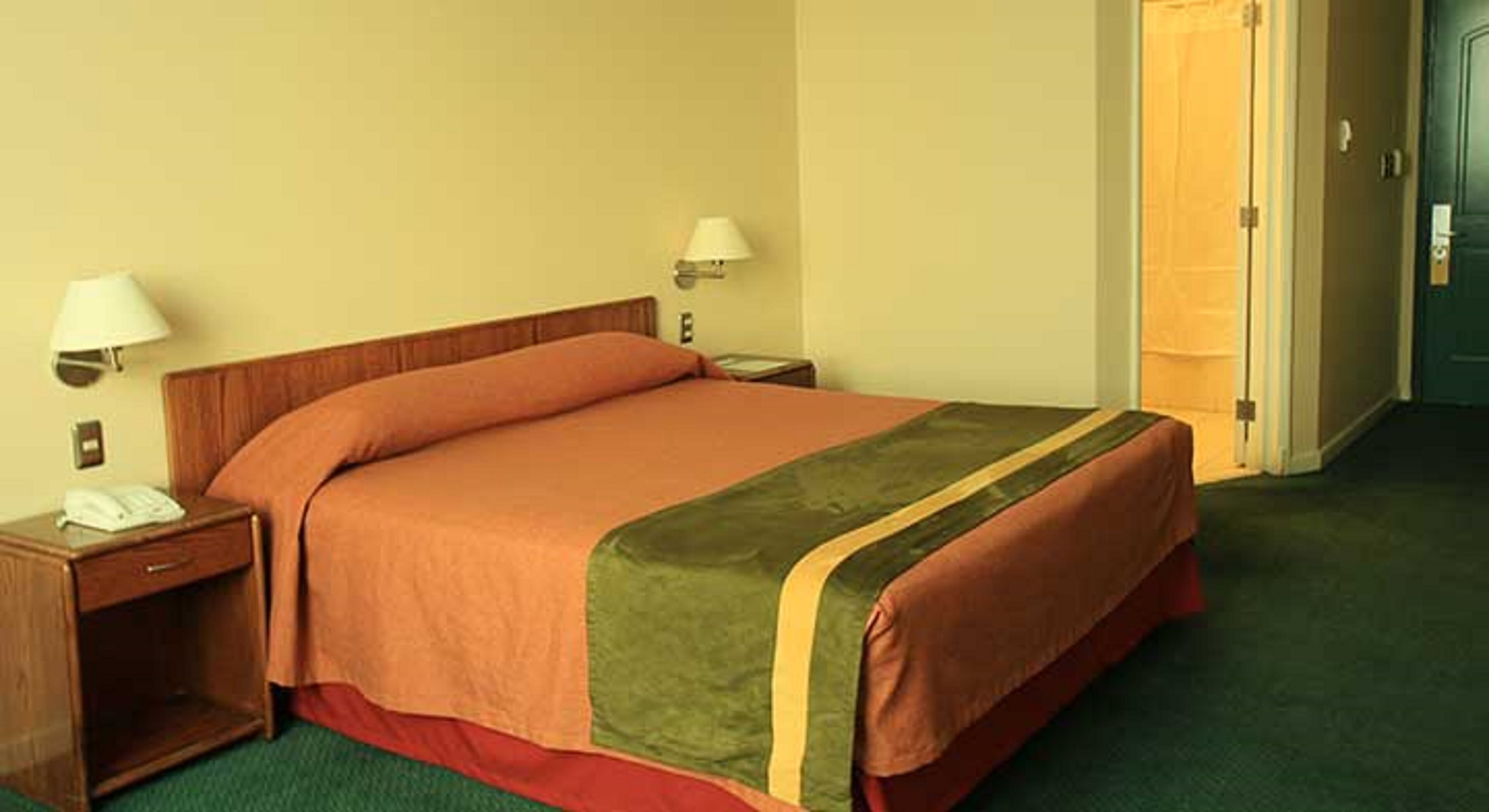 A standard hotel room with a single bed, two bedside tables, and a door to the right.