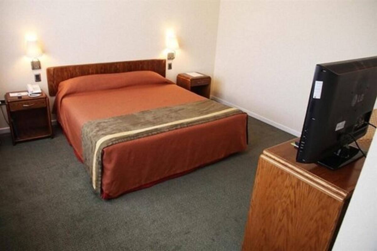 A hotel room with a bed, bedside tables, a TV, and a carpeted floor.