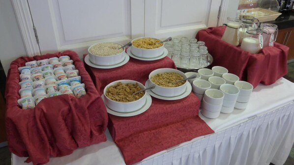 A buffet table with various food items and beverages, including bowls of cereal and milk cartons. - Hotel Diego De Almagro Concepcion (Concepción)