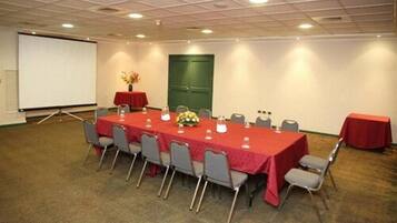 Un salón de conferencias con una larga mesa, sillas, una pantalla de proyector y una puerta verde.
