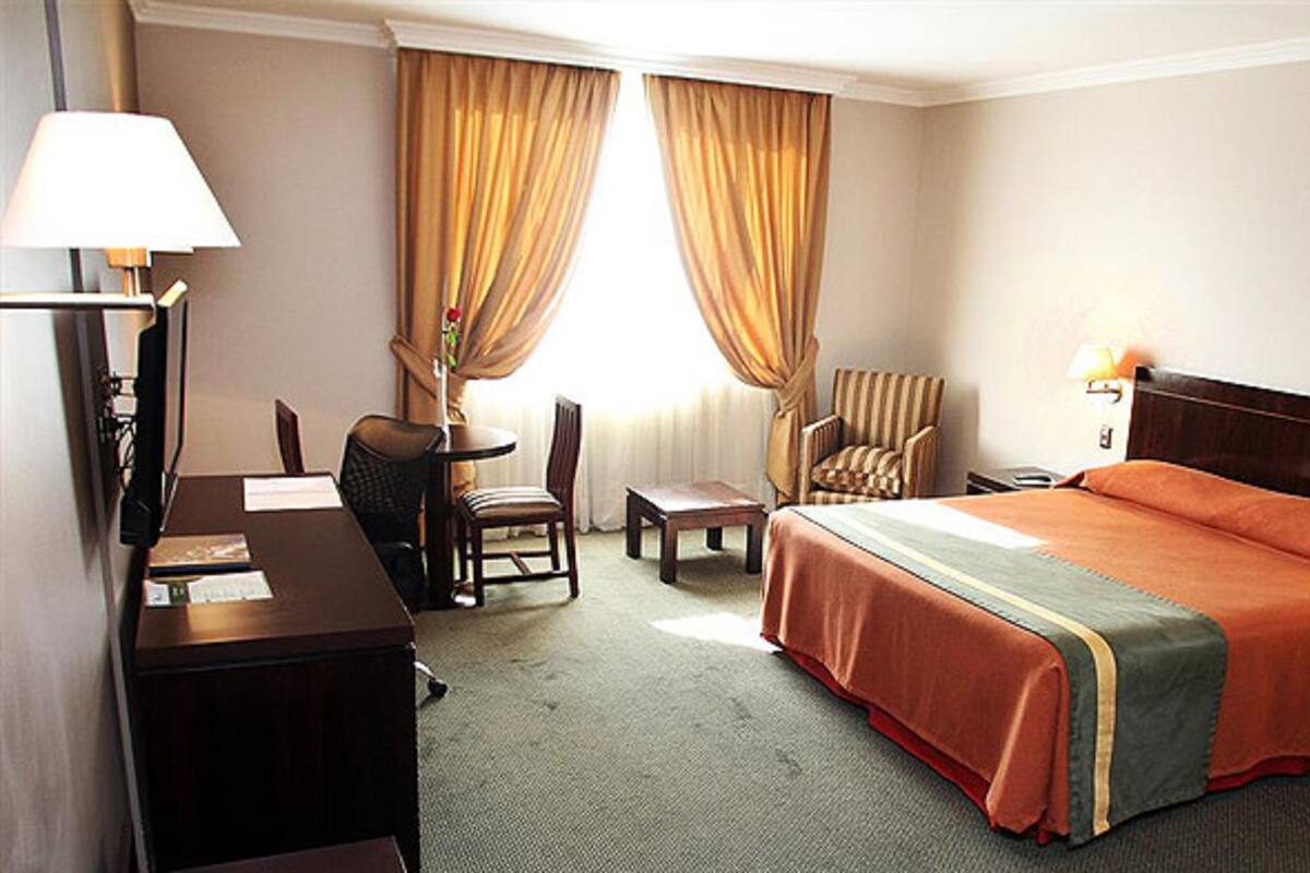 A hotel room with a bed, a desk, a chair, a lamp, and a nightstand.