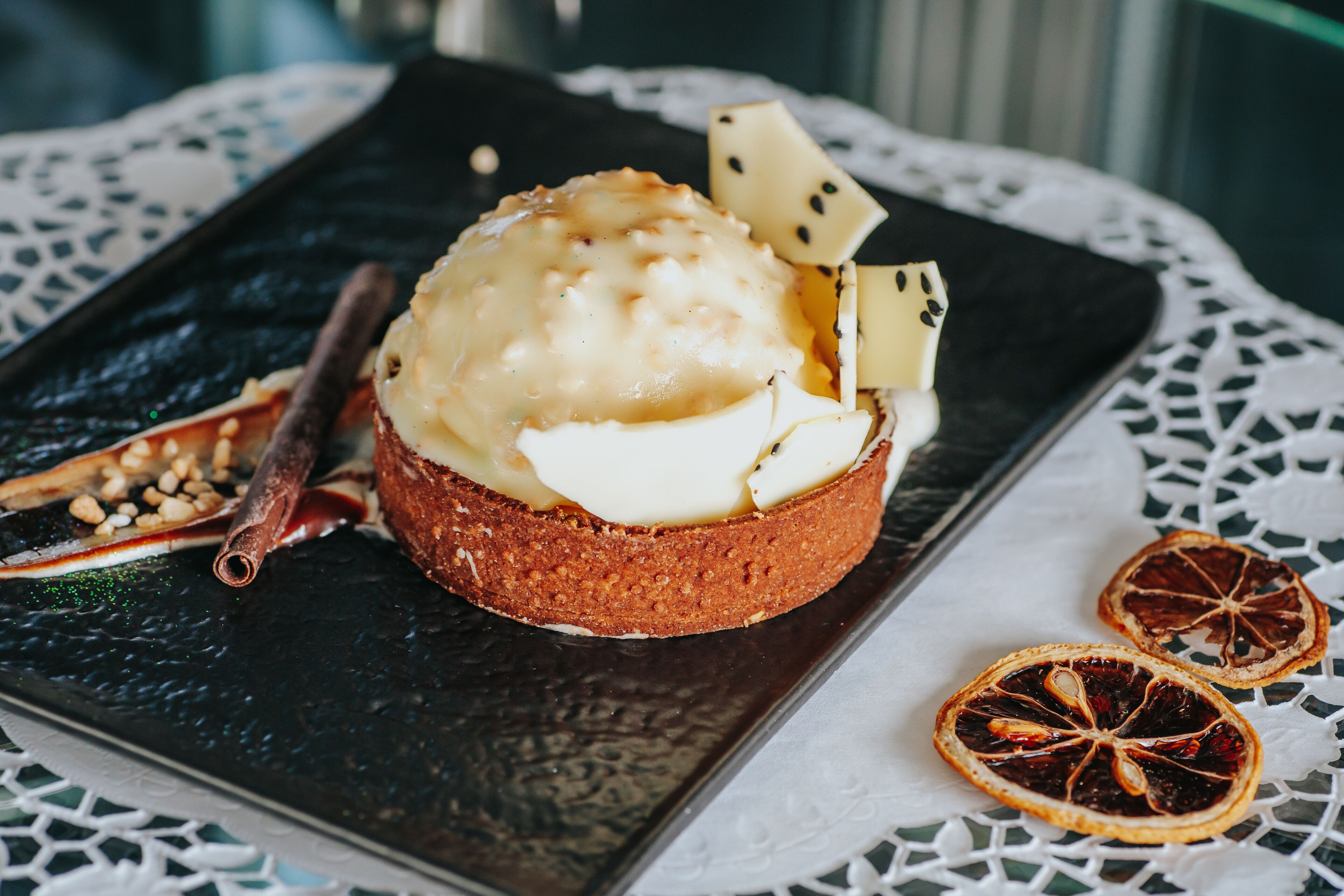 A dessert on a dark plate with dried fruit and a cinnamon stick.