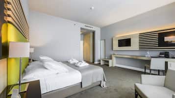 A modern hotel room with a bed, bedside table, lamp, desk, chair, and a television.