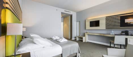 Una habitación de hotel moderna con cama, mesita de noche, lámpara, escritorio, silla y televisión.