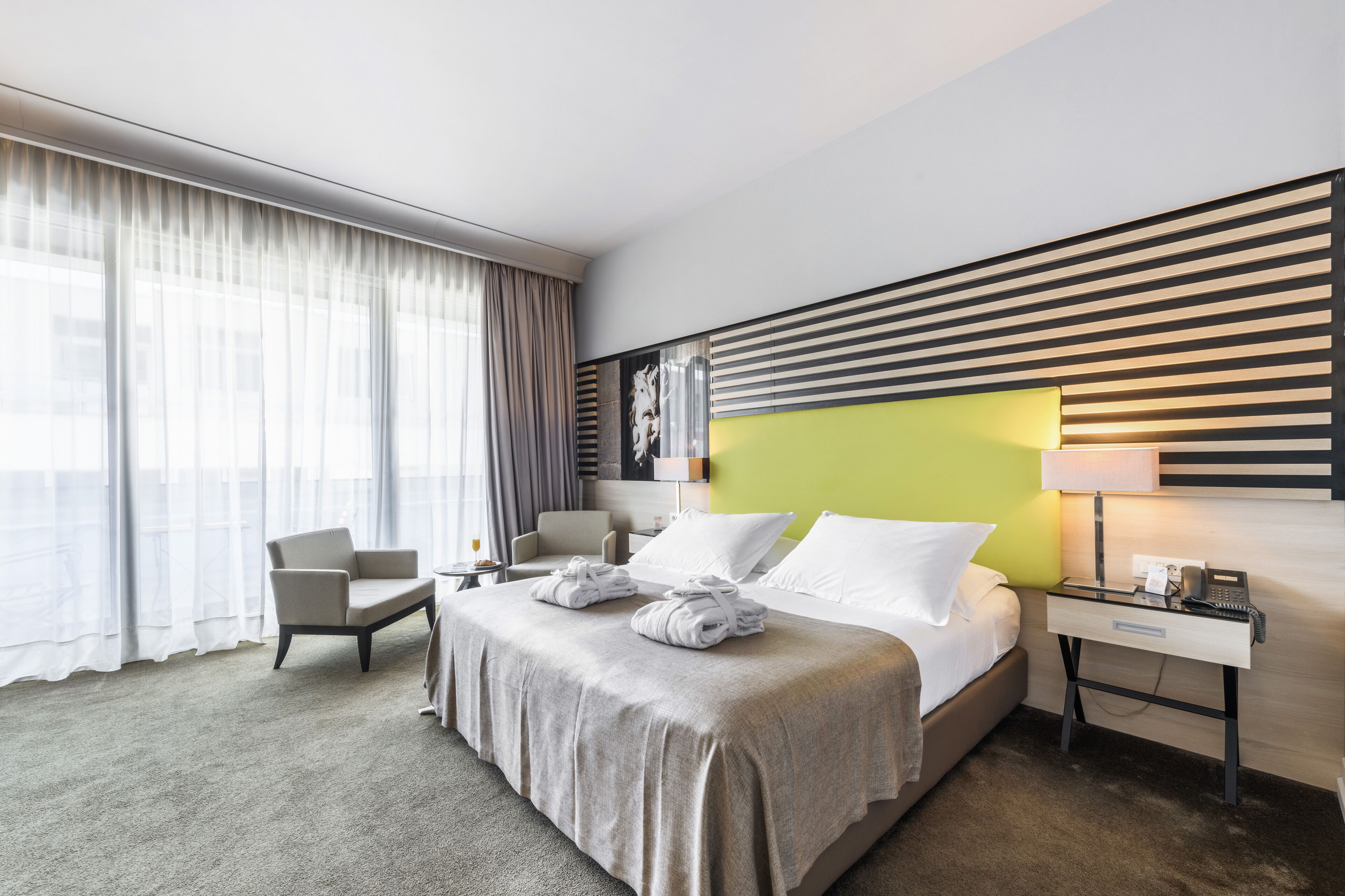 A hotel room with a large bed, a desk, a chair, and a window with curtains.