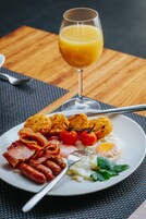 Prato de café da manhã com ovos, bacon, linguiça e tomates, acompanhado de um copo de suco de laranja.