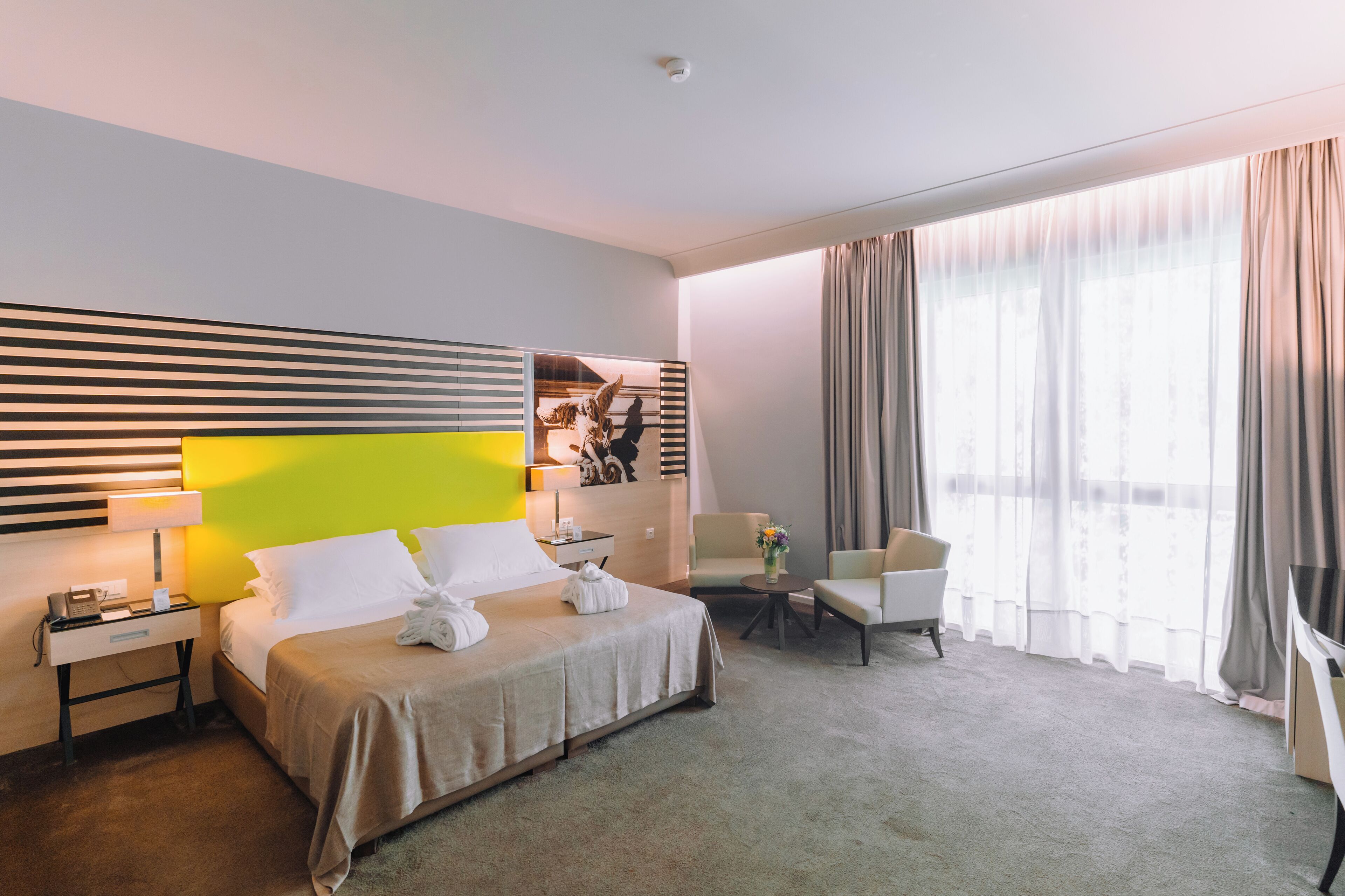 Habitación de hotel con cama, escritorio, silla, sofá y un ventanal con cortinas.