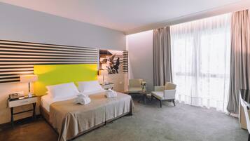 Habitación de hotel con cama, escritorio, silla, sofá y un ventanal con cortinas.