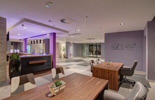 Uma sala de conferências moderna com mesa e cadeiras de madeira, um balcão de recepção e entrada por porta de vidro.