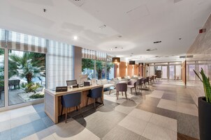 Un vestíbulo moderno de hotel con una mesa de recepción, asientos cómodos, ventanas amplias y vistas a palmeras.