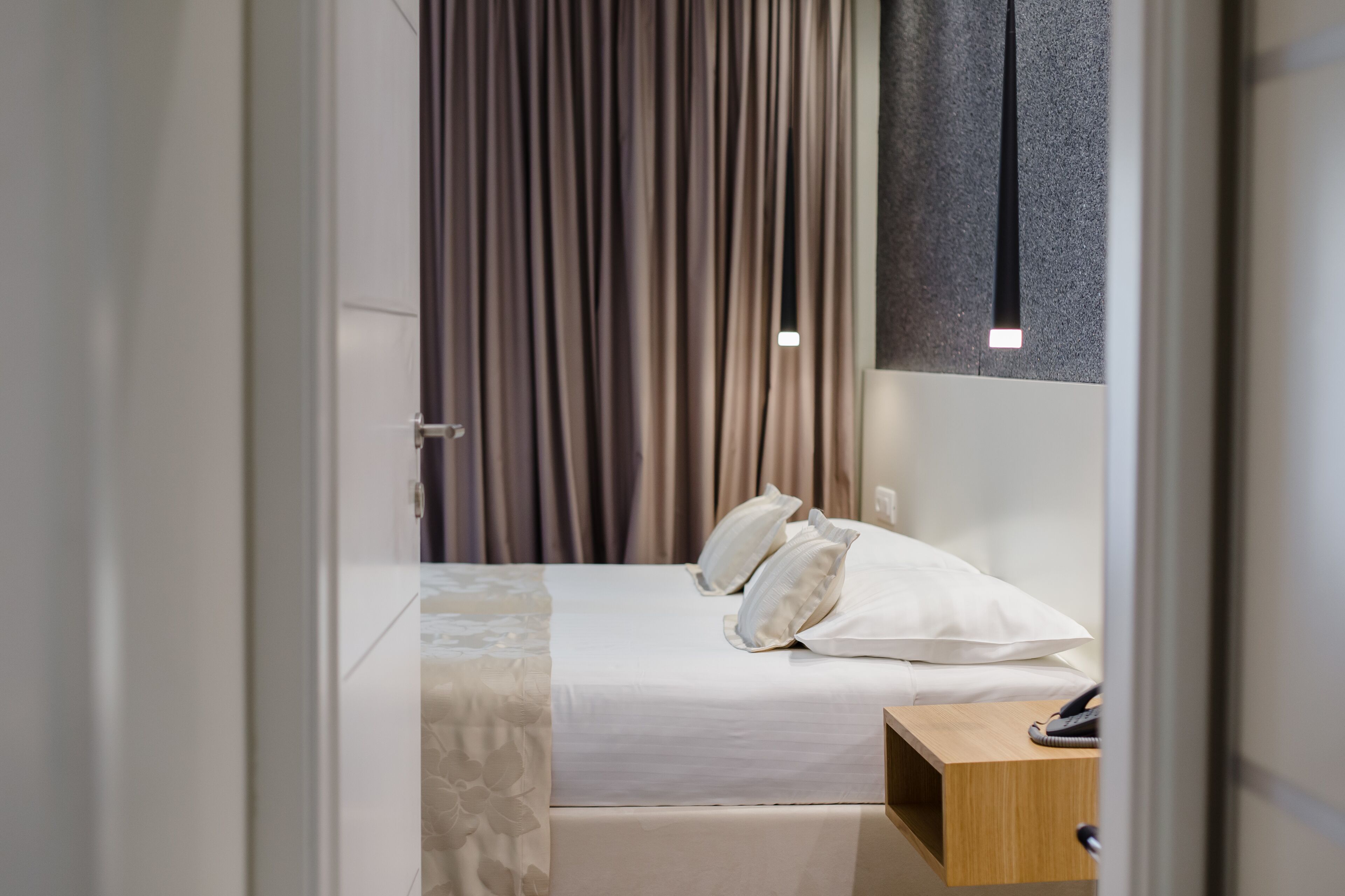 A hotel room with a bed, a bedside table, and a curtain.